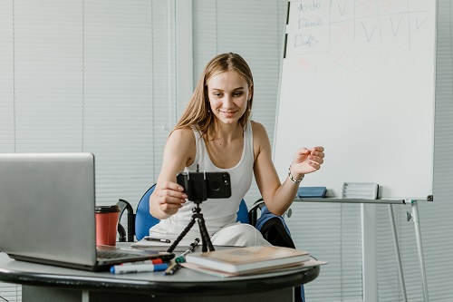 Young woman speaking in front of camera for vlog as blogger. Caucasian businesswoman working, recording video tutorial at office. Earn extra money, Side hustle, money making, turning hobbies into cash