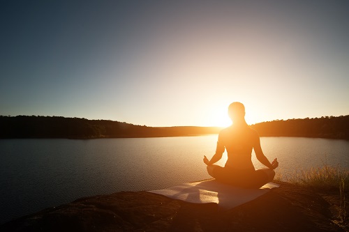 Silhouette of healthy woman is practicing yoga at mountain lake